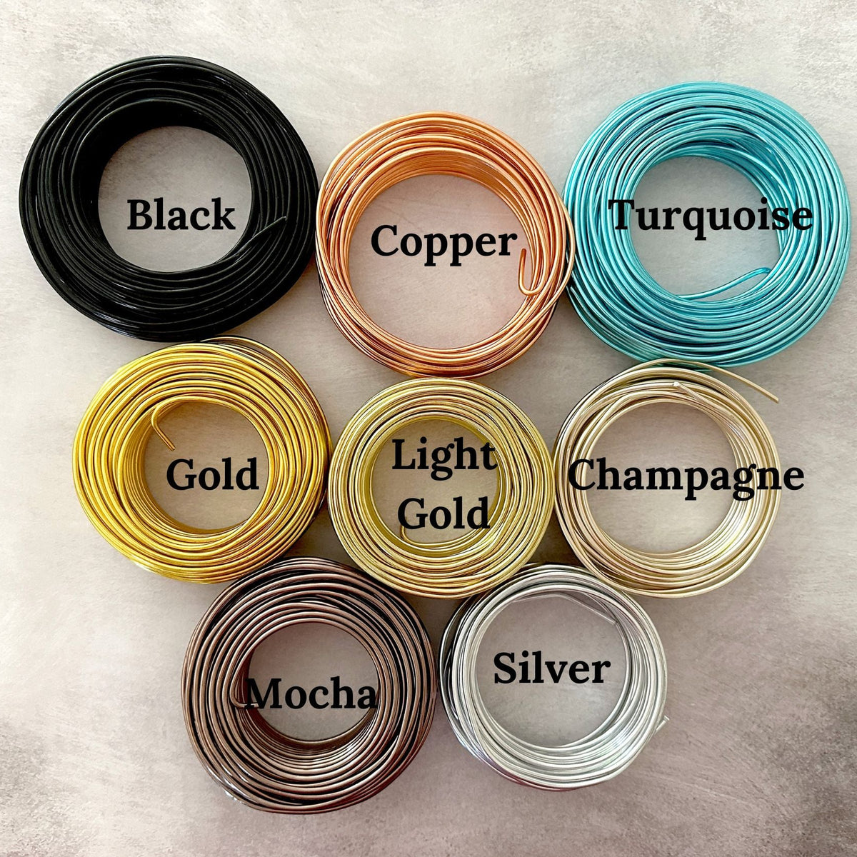 Coils of wire on a cement looking flatlay. Colors: black, copper, turquoise, gold, light gold, champagne, mocha and silver.
