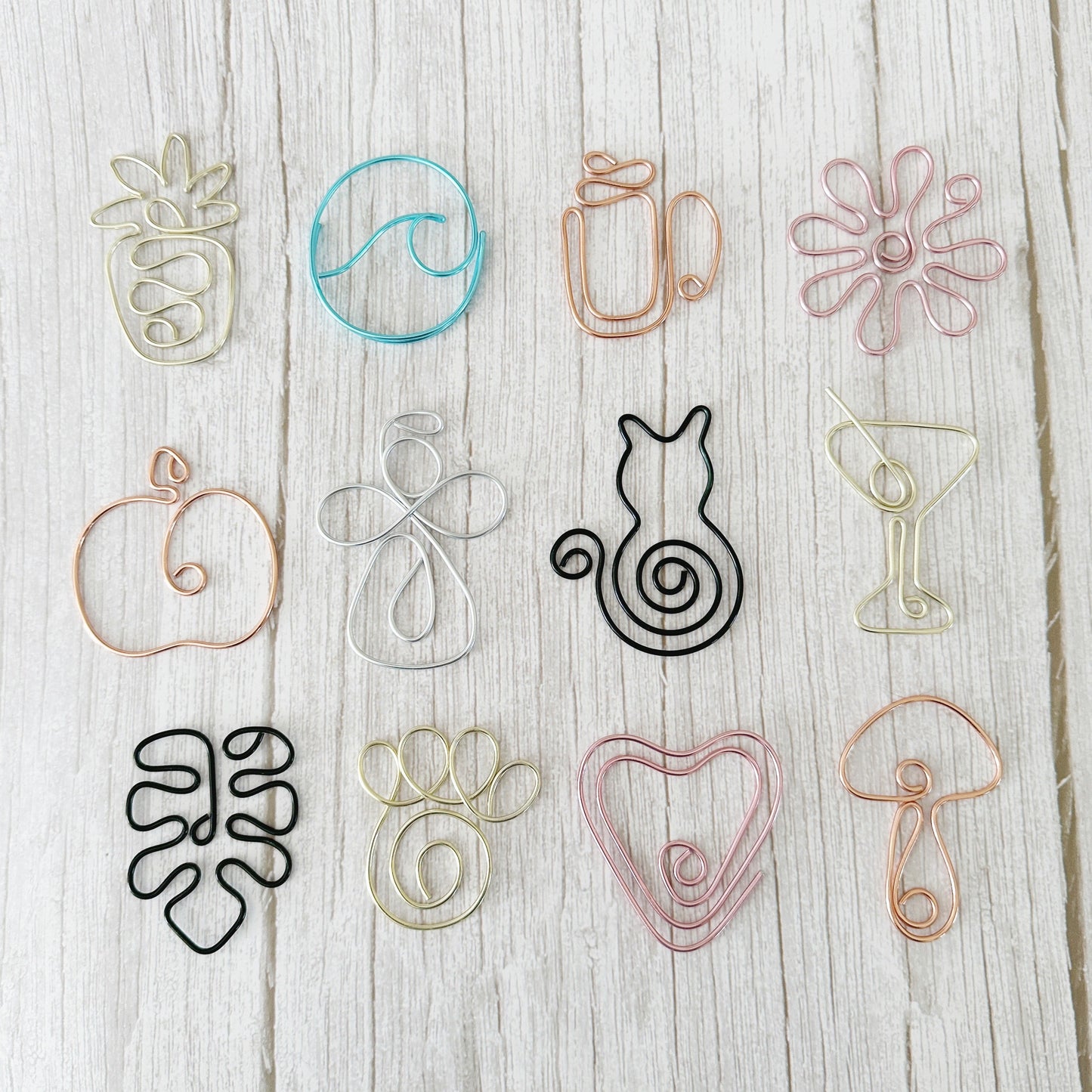Set of wire art bookmarks or planner clips in multiple colors and designs on a wooden surface