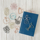 Decorative wire bookmarks on a wooden surface with a blue book.