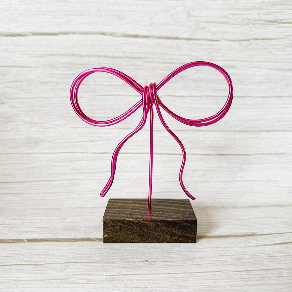 Pink wire bow on a wooden stand against a light wood panel background