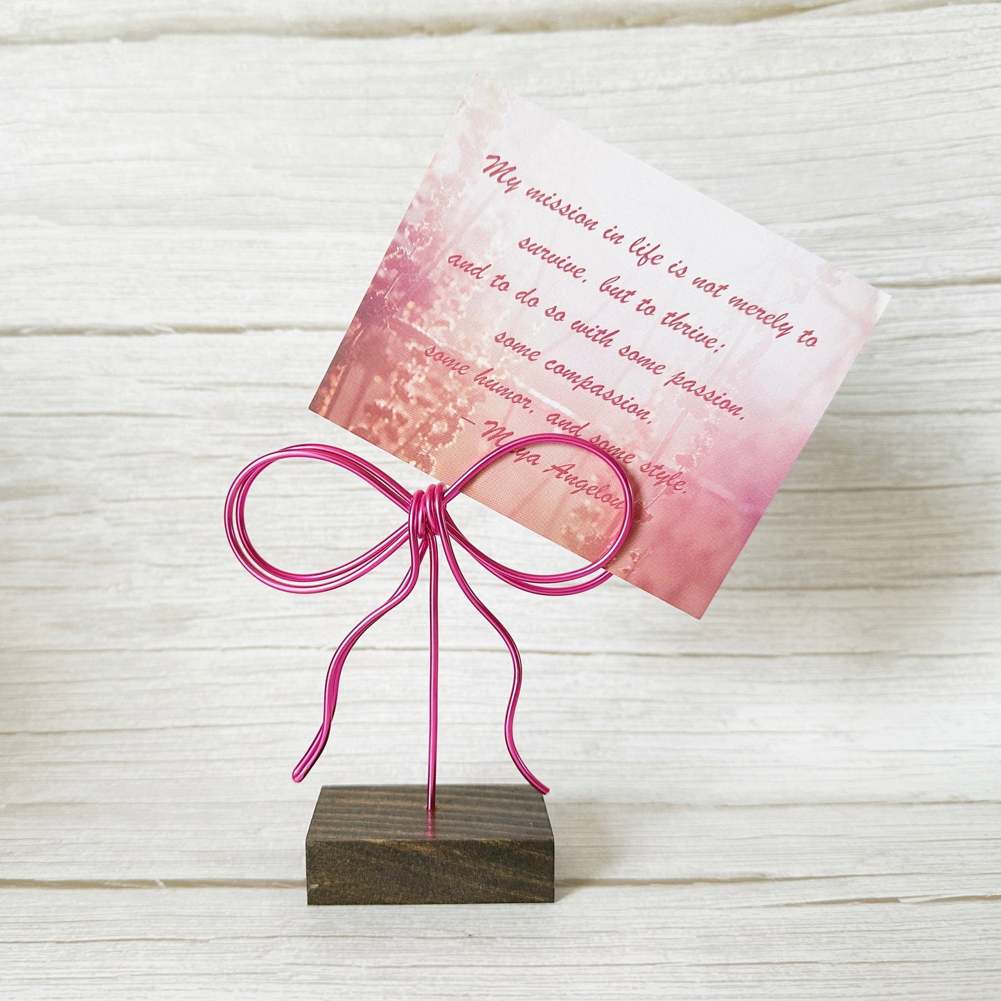 Card inserted into a wire pink bow photo holder on a wooden stand against a light wooden background