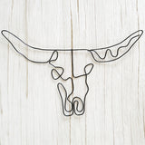 Black wire wall art shaped like a bull skull with longhorns, styled on a light wood background for modern rustic decor.