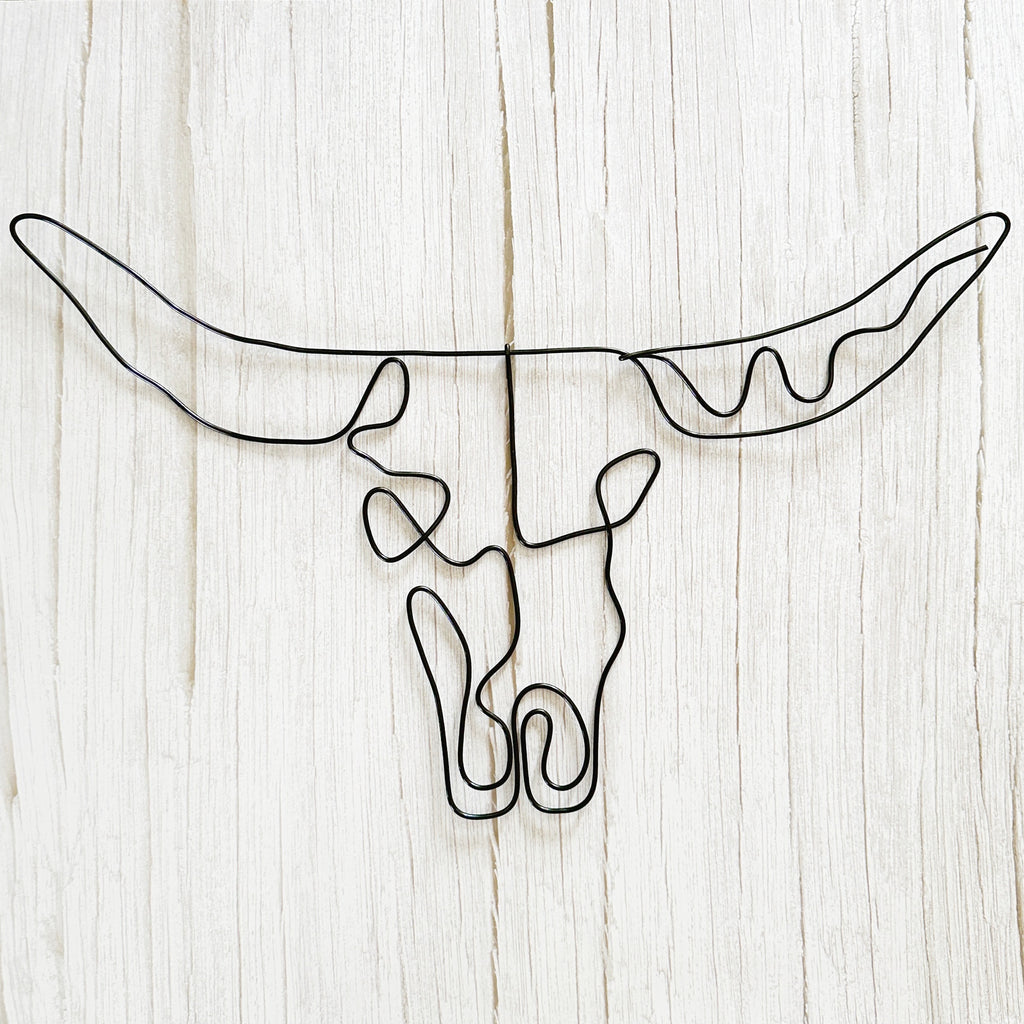 Black wire wall art shaped like a bull skull with longhorns, styled on a light wood background for modern rustic decor.