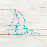 Sailboat wall decor outline made of blue wire on a light wooden surface for a coastal home, beach house or nautical theme room.