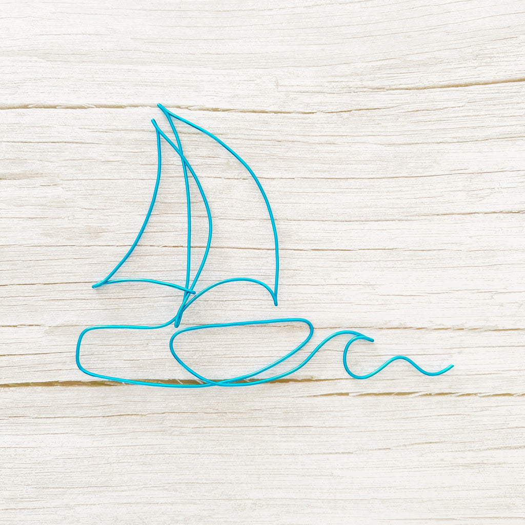 Sailboat wall decor outline made of blue wire on a light wooden surface for a coastal home, beach house or nautical theme room.
