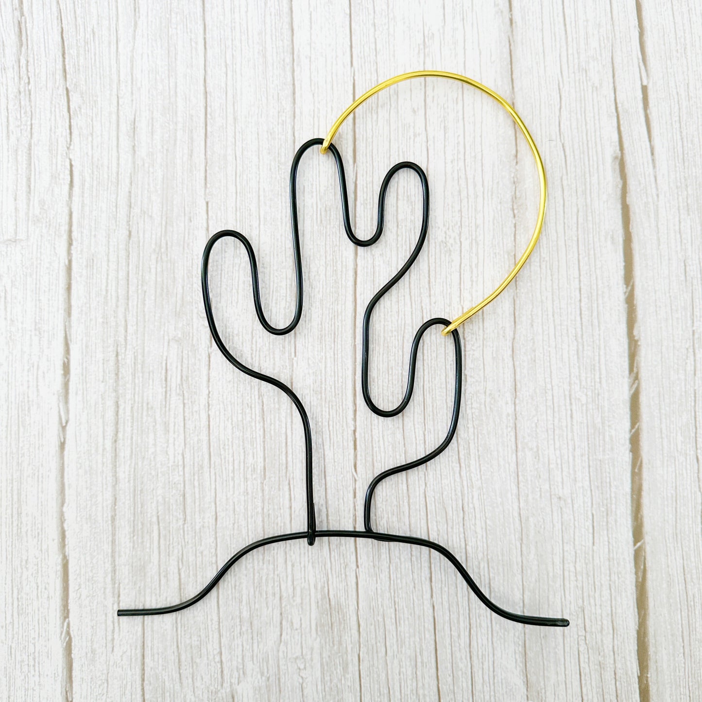 Handmade wire art of a black cactus and gold sun, styled on a light wood background—minimalist desert wall decor.