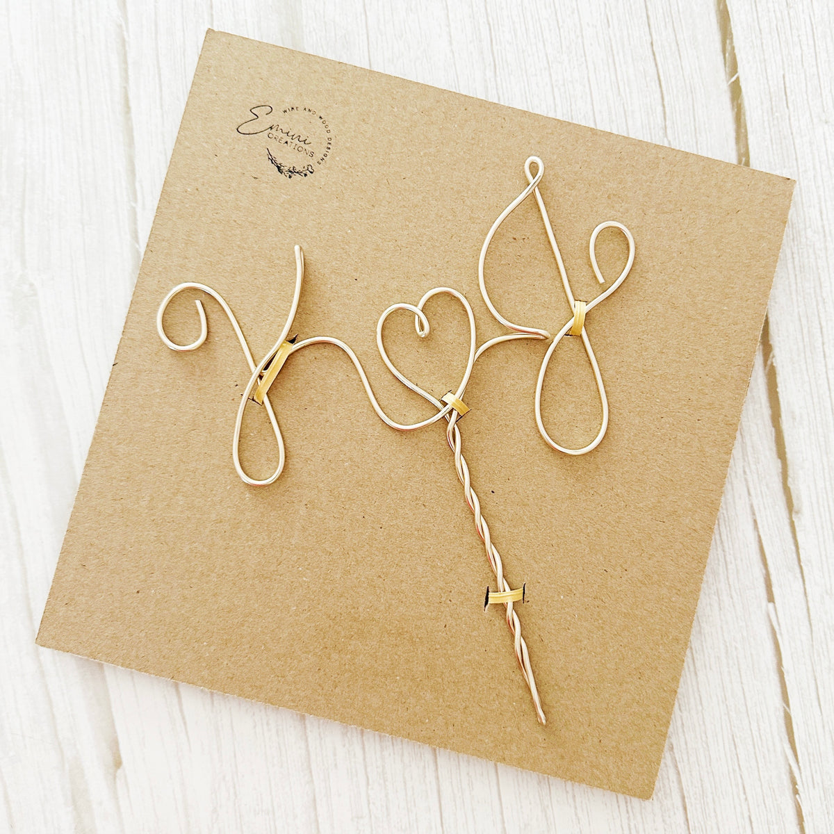 A personalized wire cake topper designed with the initials K and J with a heart shape between attached to a cardboard backing. 