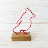 Red wire sculpture of a cardinal on a wooden base against a white background