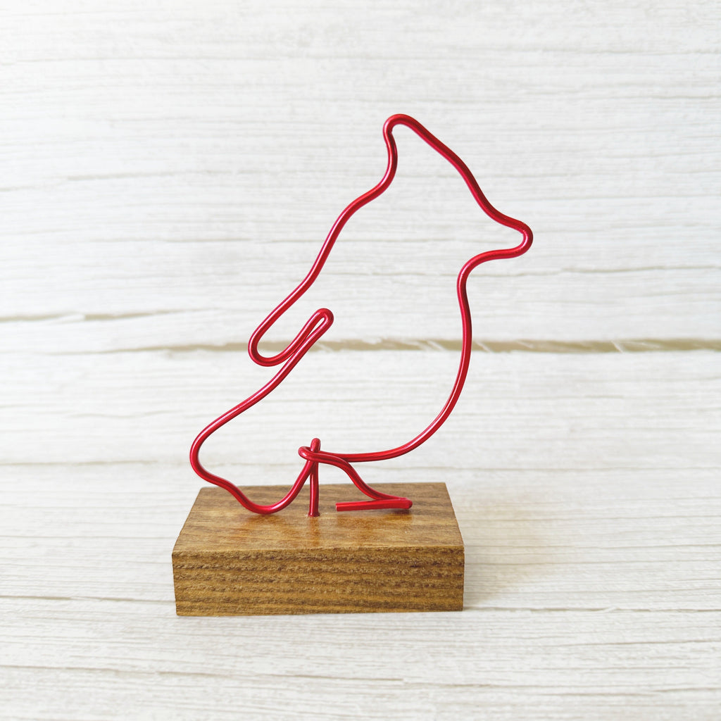 Red wire sculpture of a cardinal on a wooden base against a white background