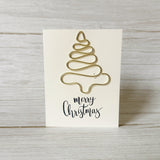 Gold Christmas tree-shaped ornament made from wire on a white card with 'merry Christmas' text, placed on a wooden surface.