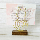Gold wire cat-shaped photo holder with a spiral tail, mounted on a wood base, holding a quote card on a light wood background.