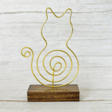 Gold wire cat-shaped photo holder with a spiral tail, mounted on a wood base sitting on a light wood background.