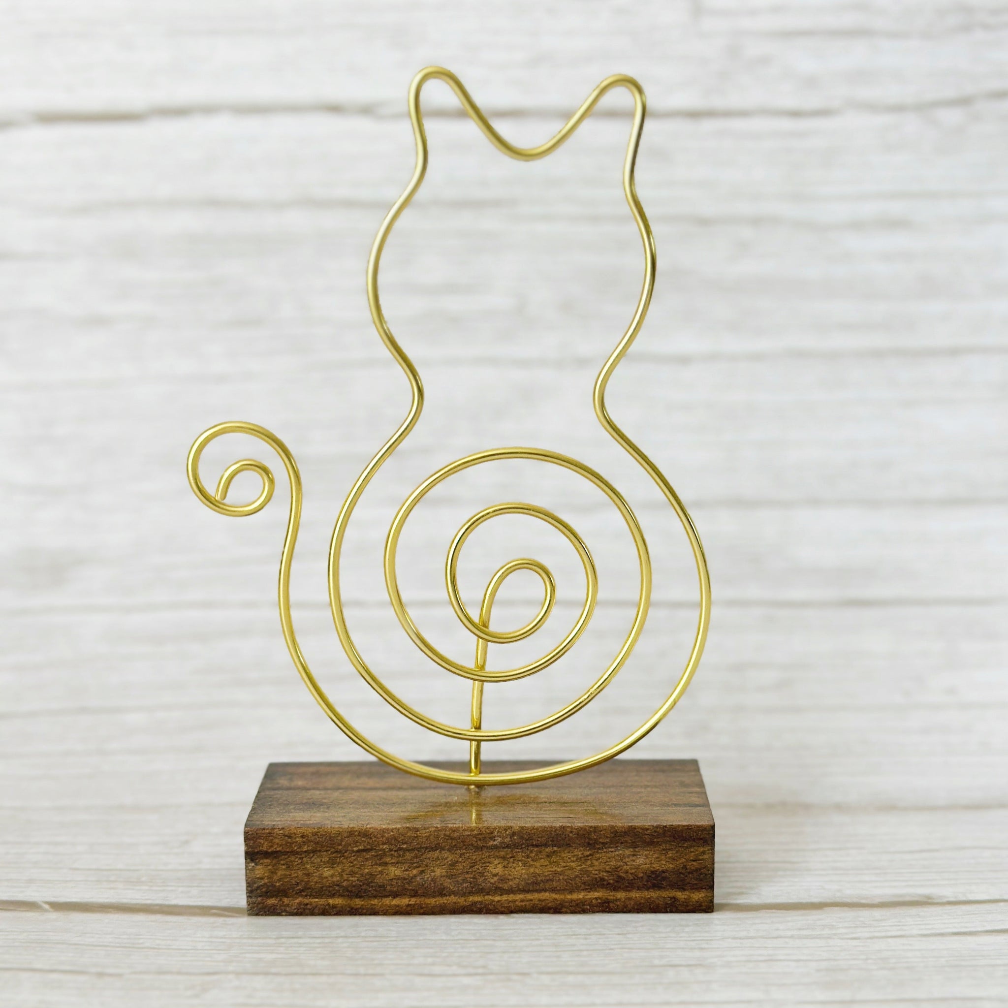 Gold wire cat-shaped photo holder with a spiral tail, mounted on a wood base sitting on a light wood background.