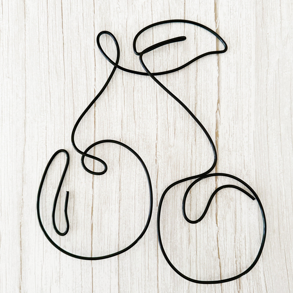 Minimalist cherry wall art made from black wire, shaped into two cherries with a leaf, styled on a light wood background.
