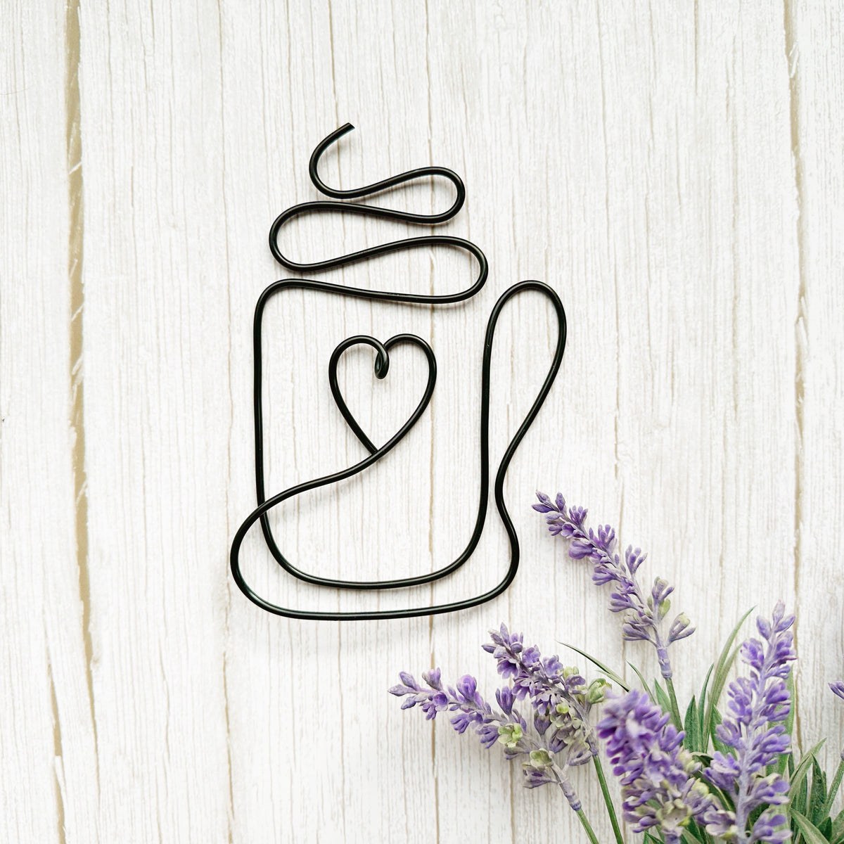 Decorative metal coffee mug wall art with a heart design on a wooden surface with lavender flowers.