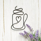 Decorative metal coffee mug wall art with a heart design on a wooden surface with lavender flowers.