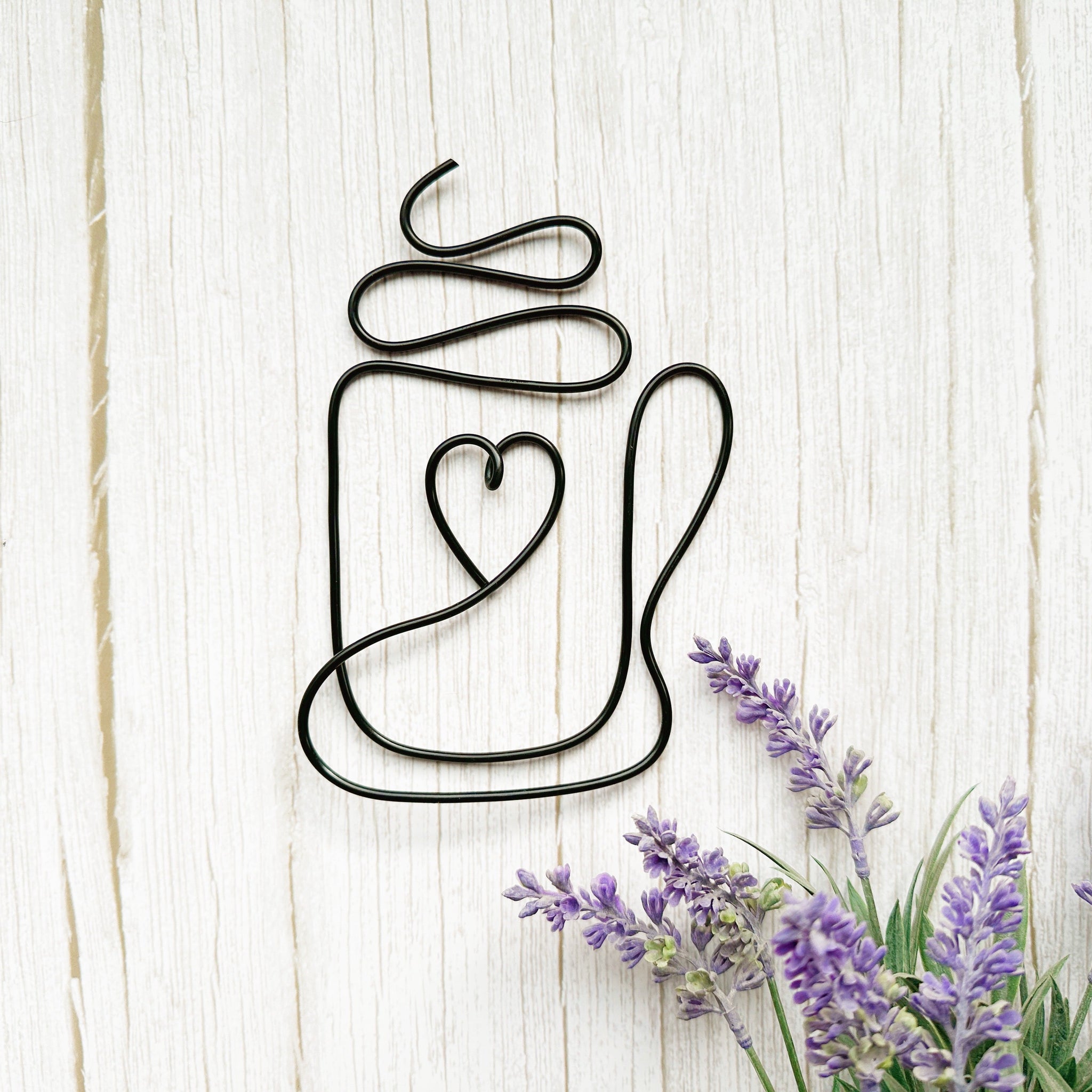 Decorative metal coffee mug wall art with a heart design on a wooden surface with lavender flowers.