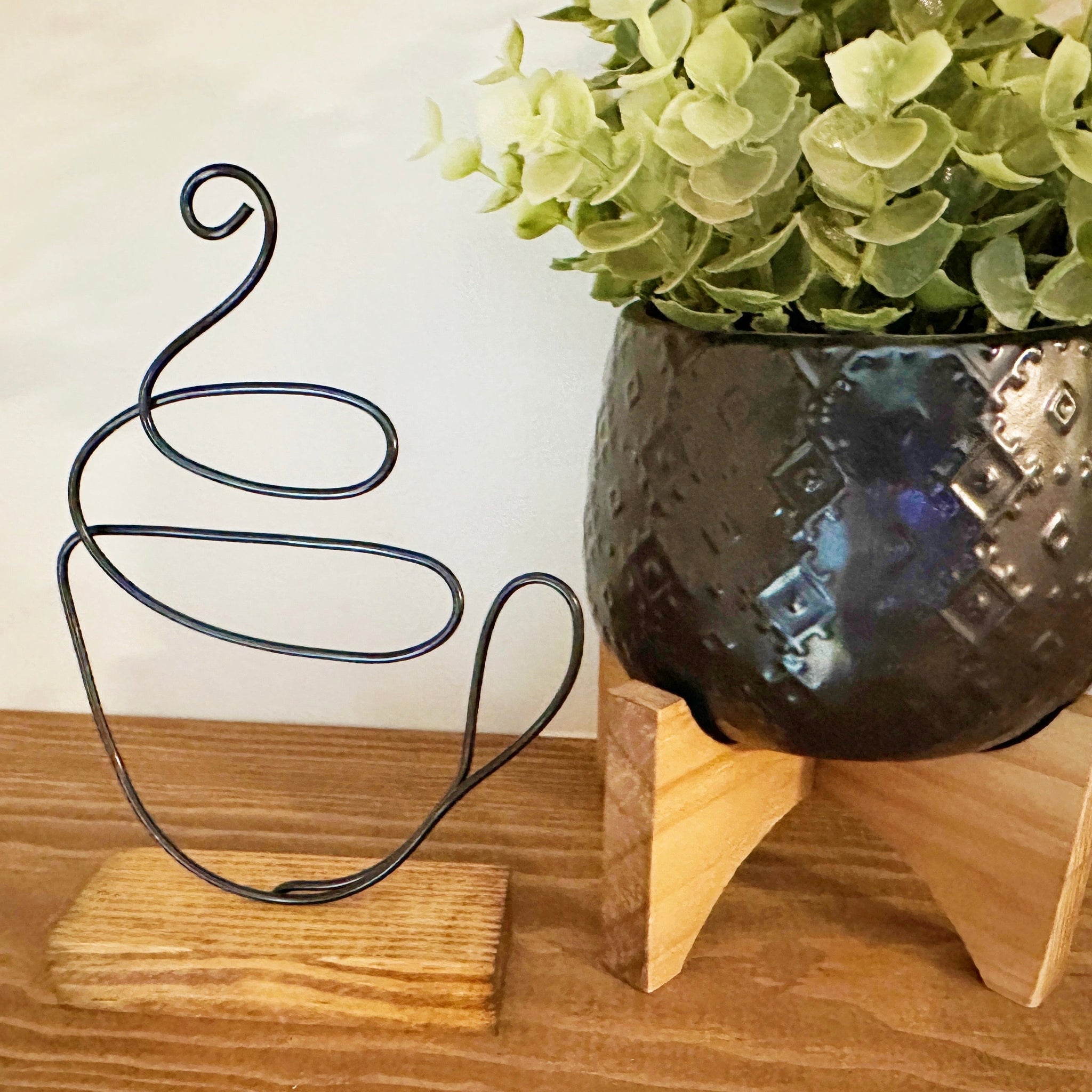 Decorative faux plant next to a wire coffee mug sculpture on a wooden surface