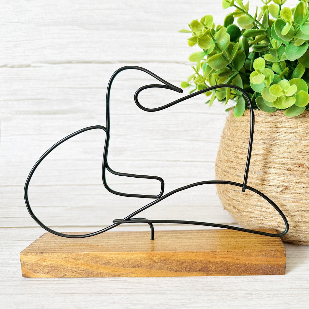 Decorative wire cowboy hat sculpture on a wooden base with a potted plant in the background