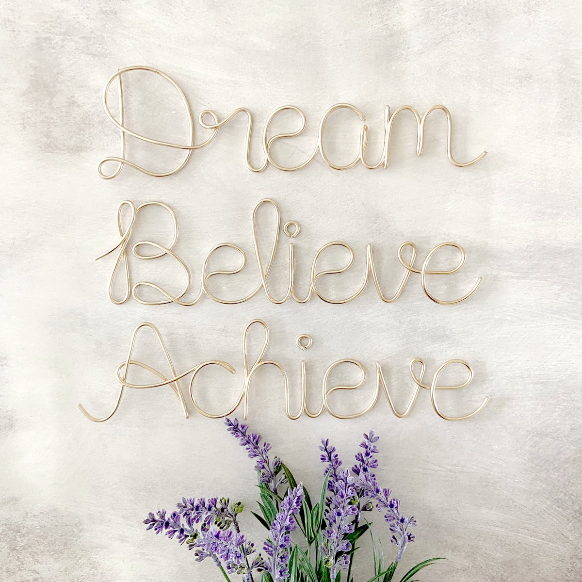 A motivational sign reading 'DREAM BELIEVE ACHIEVE' in a cursive font, with a decorative purple flower at the bottom.