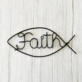 Minimalist wire wall art in the shape of the Christian Ichthus fish symbol with the word “Faith” in black wire, displayed on a white wall.