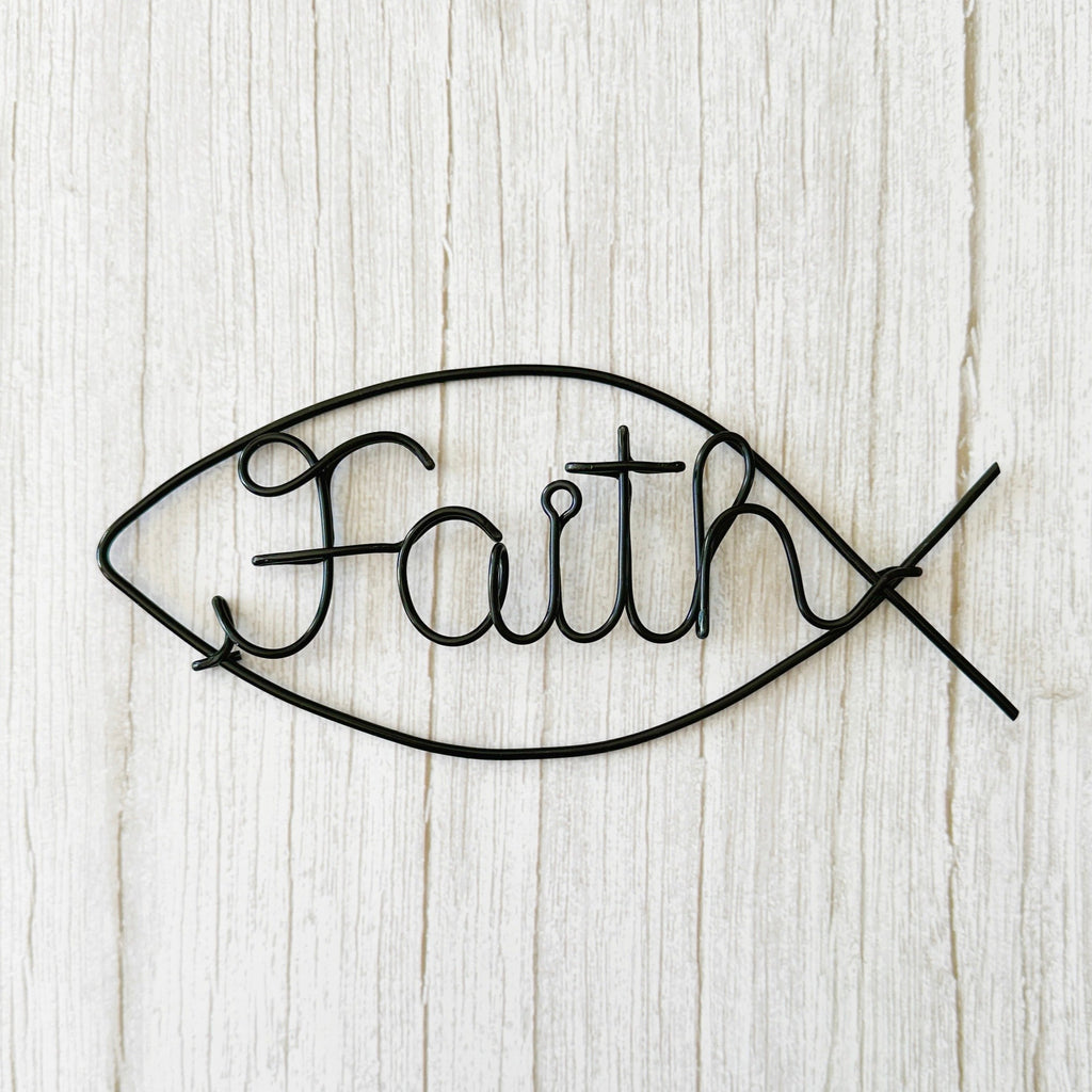 Minimalist wire wall art in the shape of the Christian Ichthus fish symbol with the word “Faith” in black wire, displayed on a white wall.