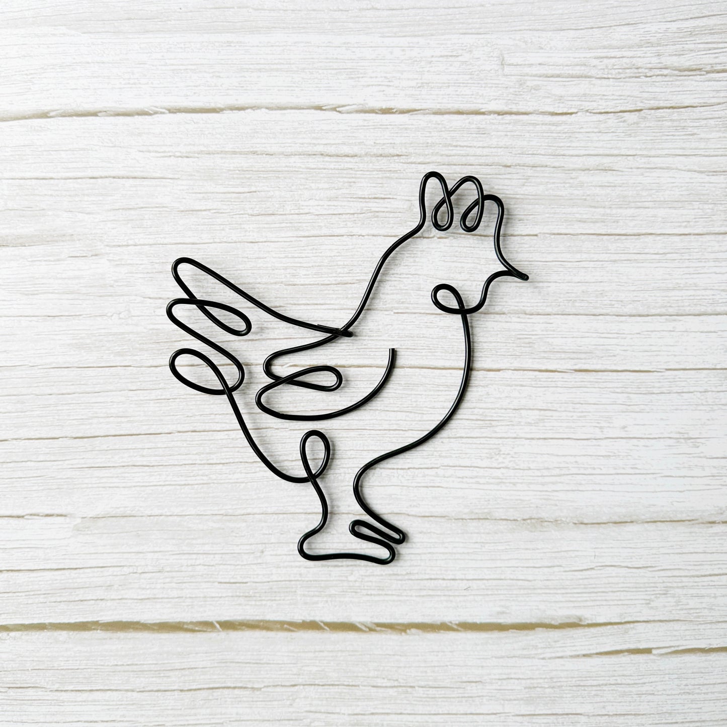 Black wire sculpture of a rooster on a light wooden background