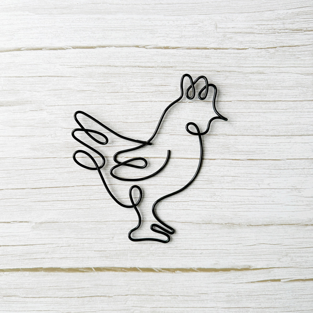 Black wire sculpture of a rooster on a light wooden background