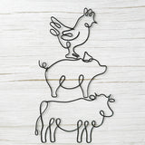 Black wire wall art featuring stacked farm animals: a chicken on a pig on a cow, styled against a rustic light wood background.