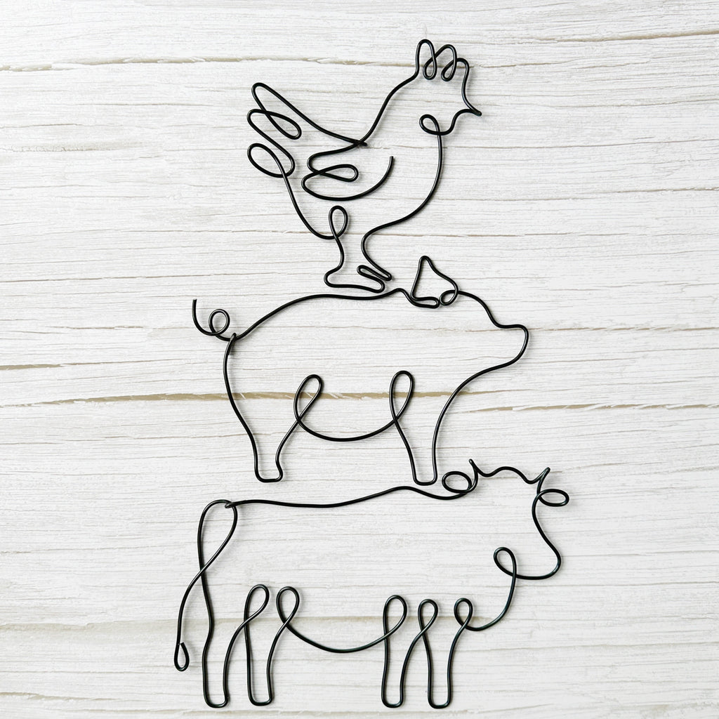 Black wire wall art featuring stacked farm animals: a chicken on a pig on a cow, styled against a rustic light wood background.