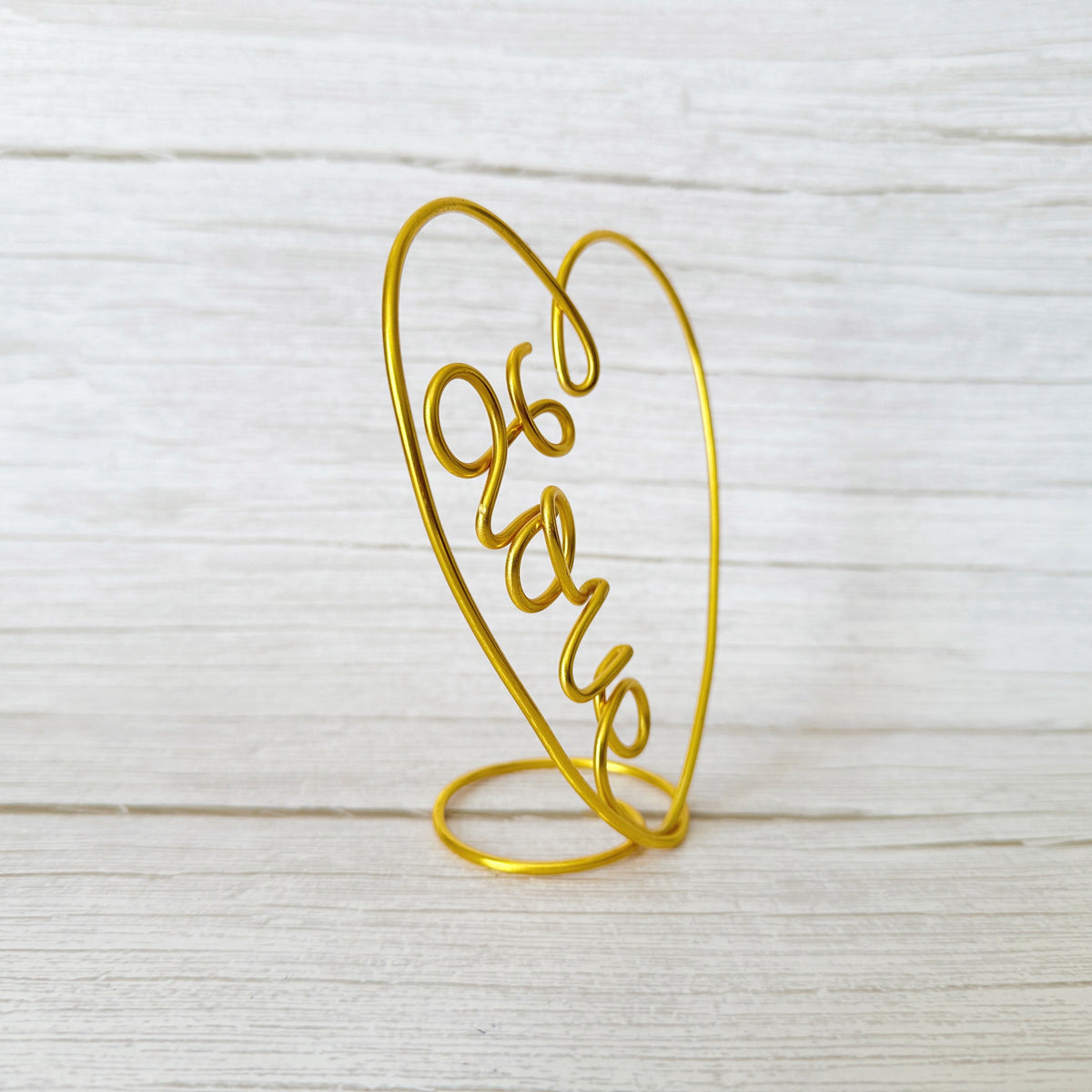 Gold heart-shaped wire sculpture with 'love' on a light wooden background