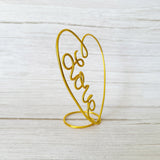 Gold heart-shaped wire sculpture with 'love' on a light wooden background
