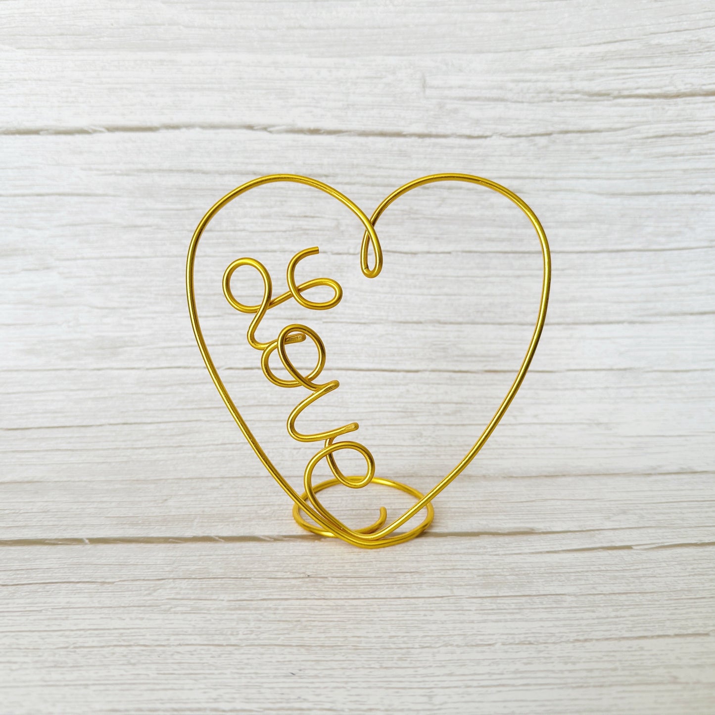 Gold wire heart-shaped holder with 'love' text on a light wooden surface