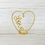 Gold wire heart-shaped holder with 'love' text on a light wooden surface