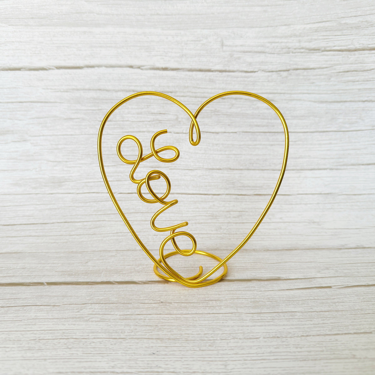 Gold wire heart-shaped holder with 'love' text on a light wooden surface