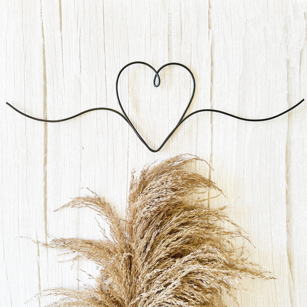 Decorative wire heart shape on a wooden background with pampas grass.