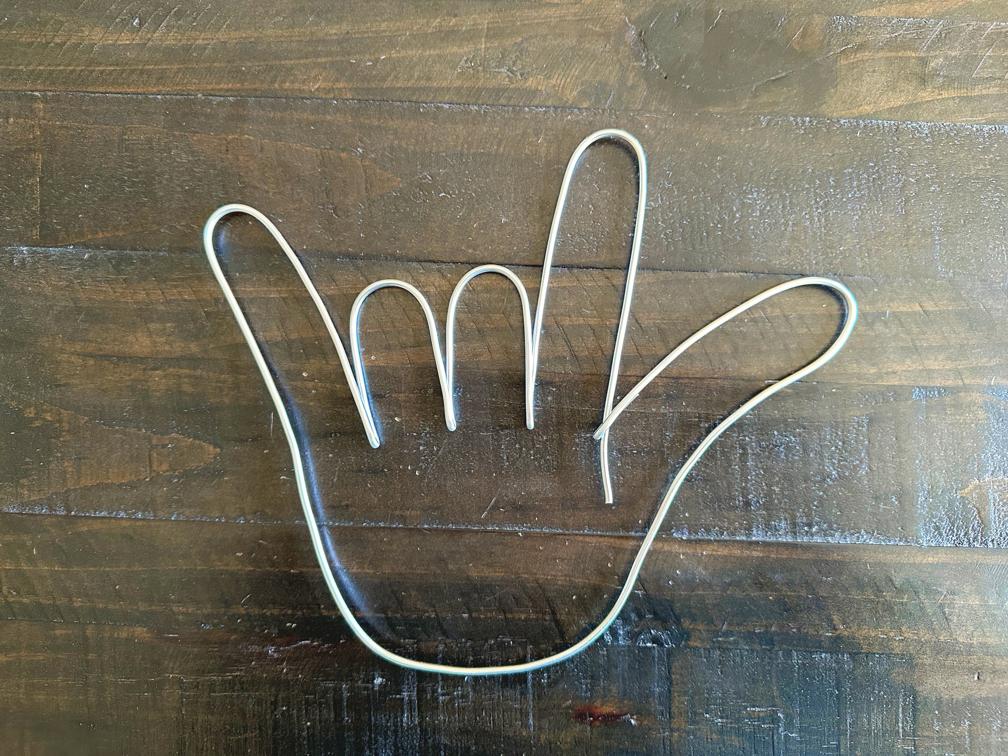 Silver wire hand shape on a dark wooden background