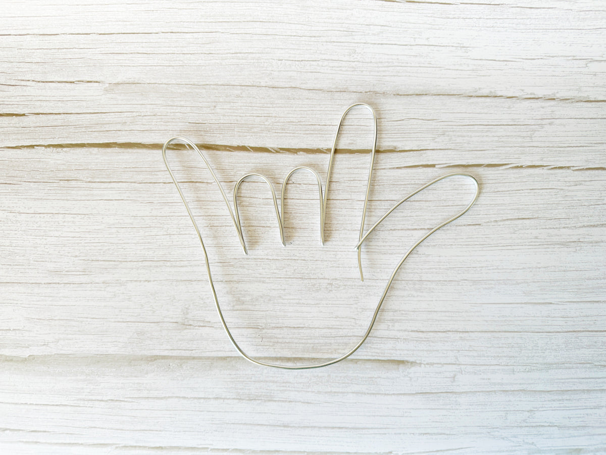 I love you hand shape made with silver colored wire laying on a light wood background.
