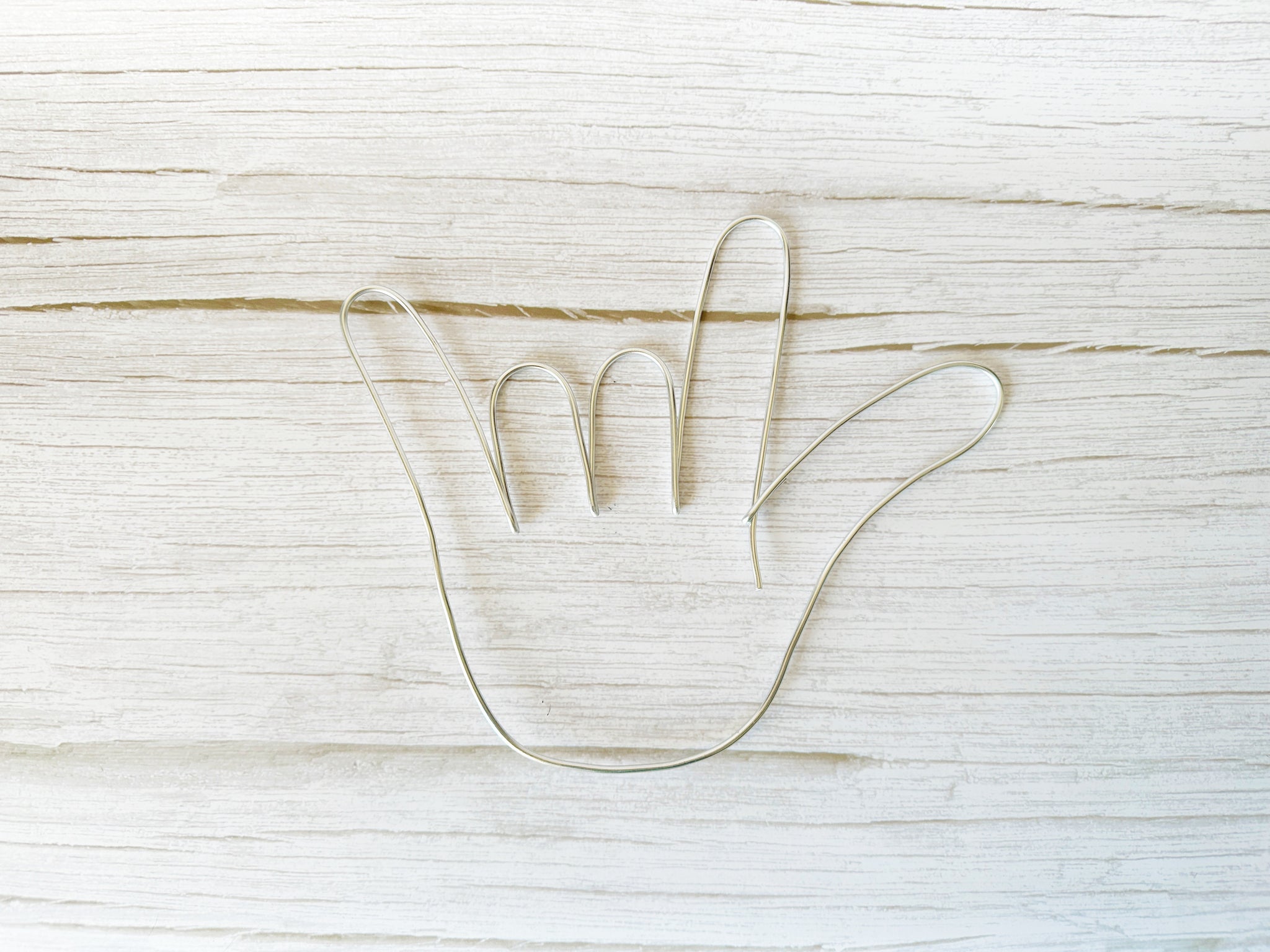 I love you hand shape made with silver colored wire laying on a light wood background.

