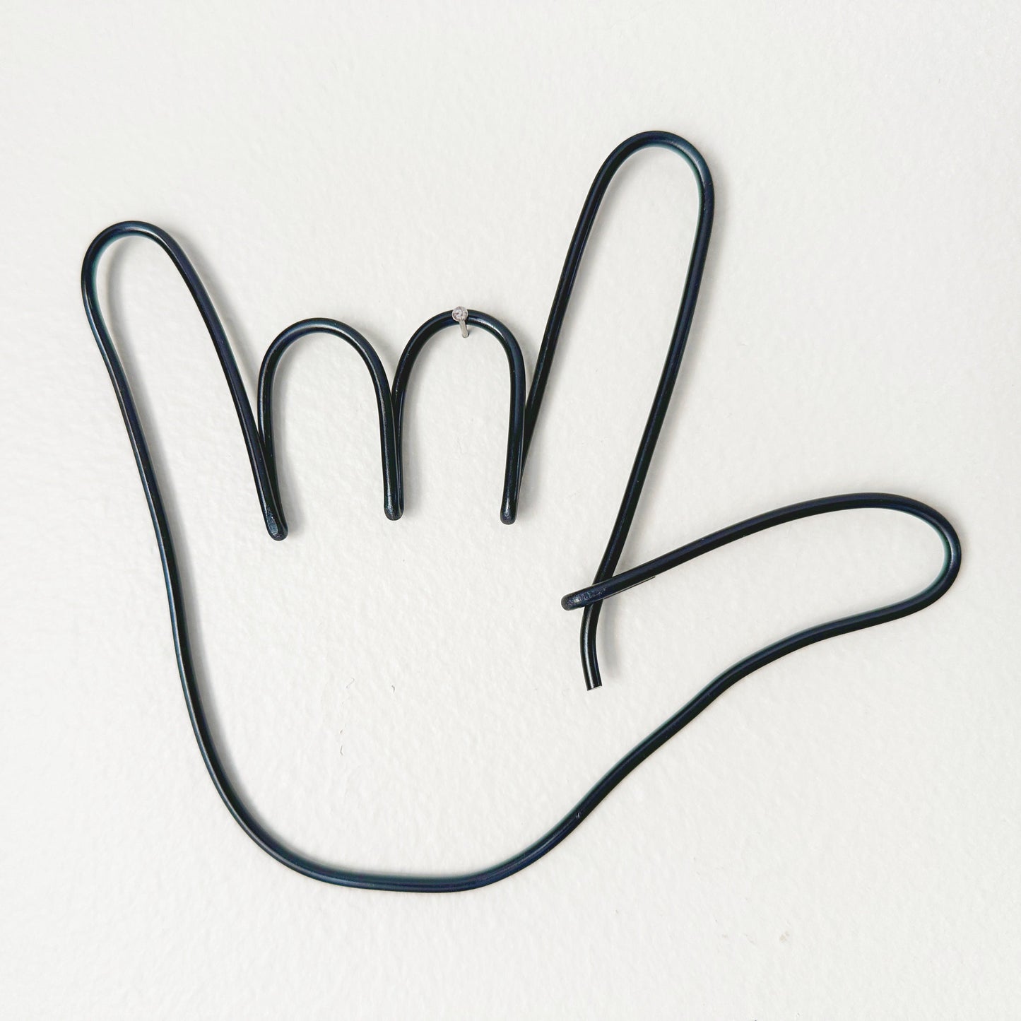 Black wire shaped like a hand hanging from a tiny nail on a wall