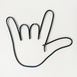 Black wire shaped like a hand hanging from a tiny nail on a wall
