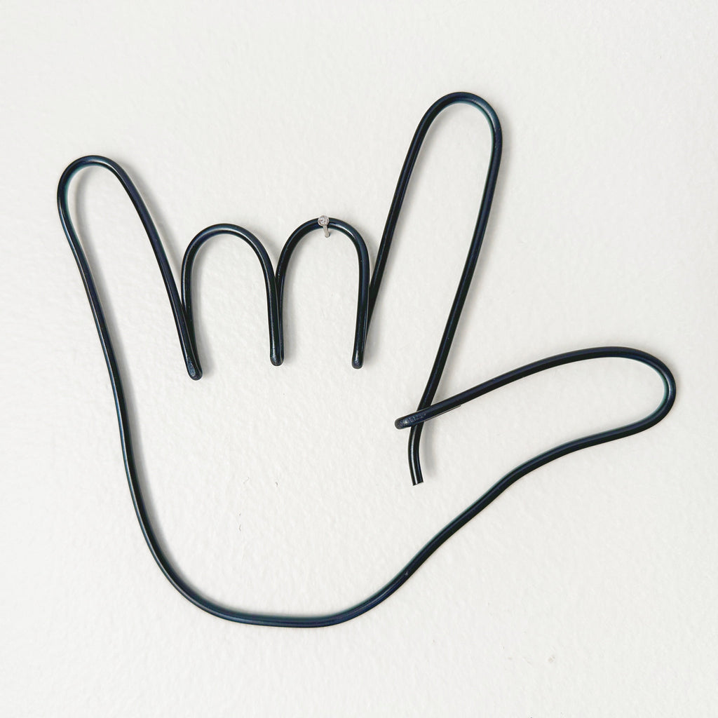 Black wire shaped like a hand hanging from a tiny nail on a wall