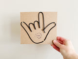 Black wire hand shaped on a cardboard backing to prepare for shipping.