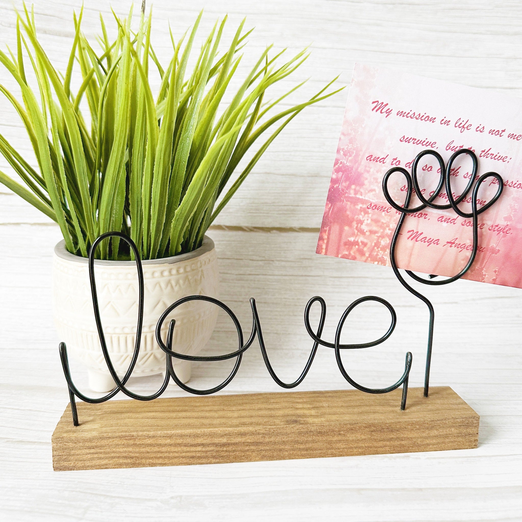 Decorative wire sign with 'love' and a paw photo holder on a wooden base, next to a potted plant and a pink card.