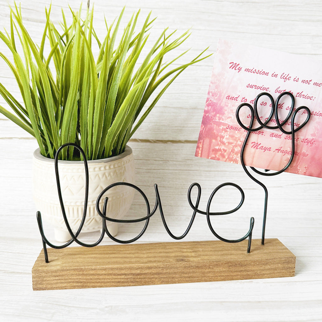Decorative wire sign with 'love' and a paw photo holder on a wooden base, next to a potted plant and a pink card.