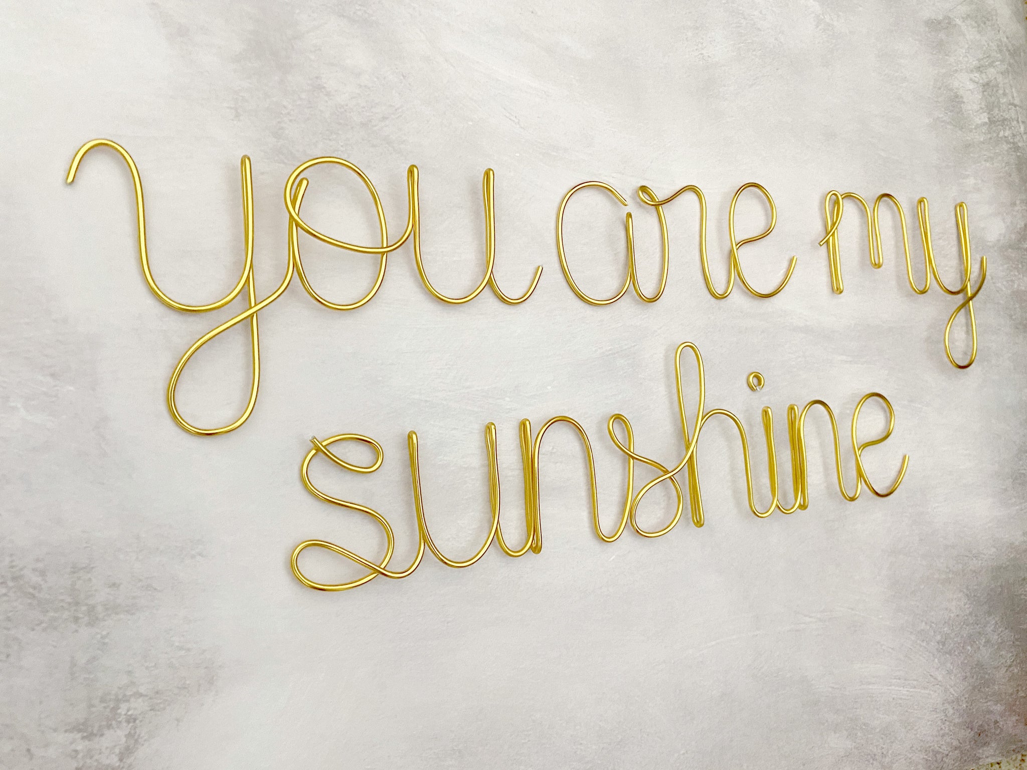 A wire wall decor that spells out 'you are my sunshine' in cursive and print lettering, displayed against a concrete background.