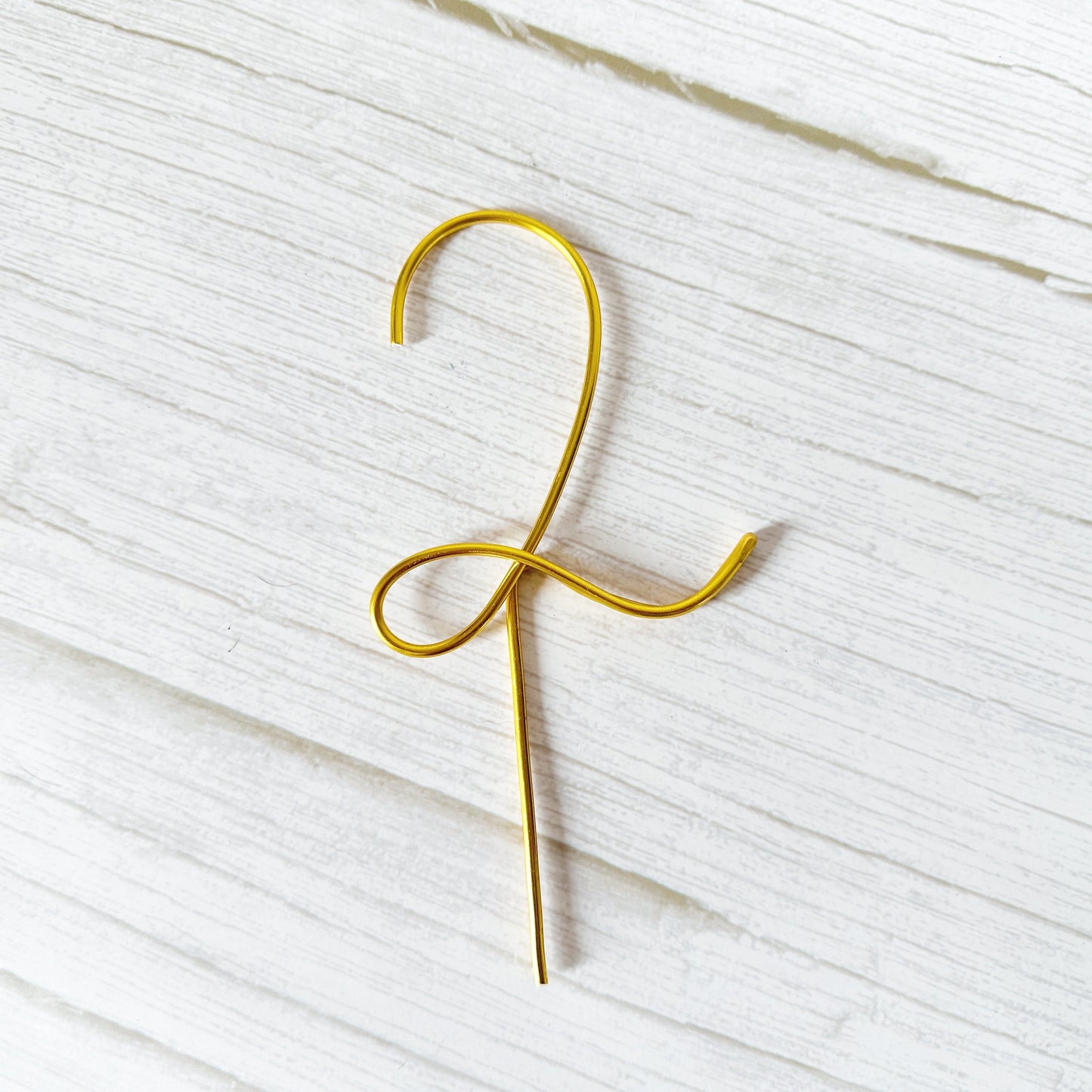 Gold wire number 2 cake topper on a white textured surface