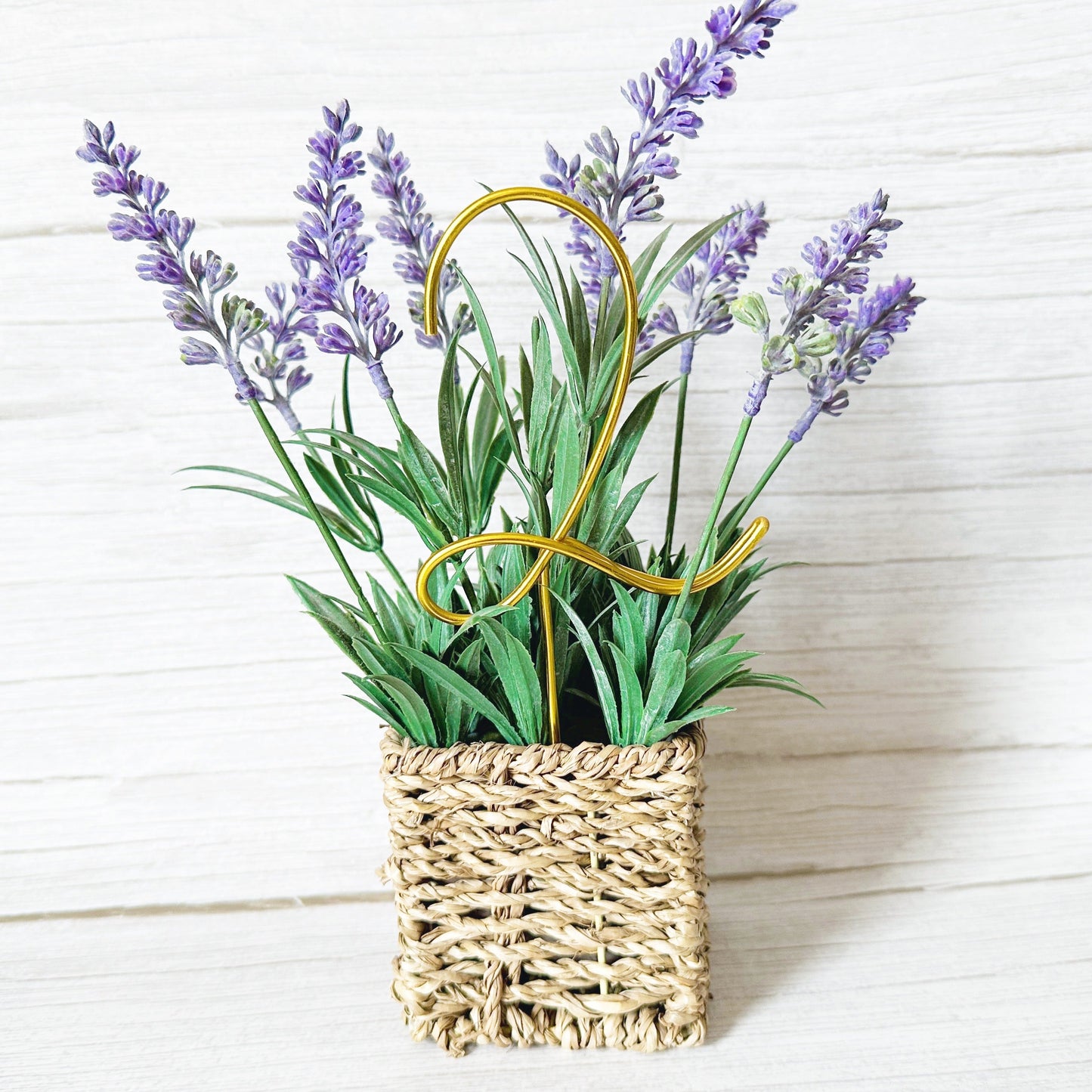Decorative basket with lavender and greenery with a gold wire number 2 plant stake on a white wooden background