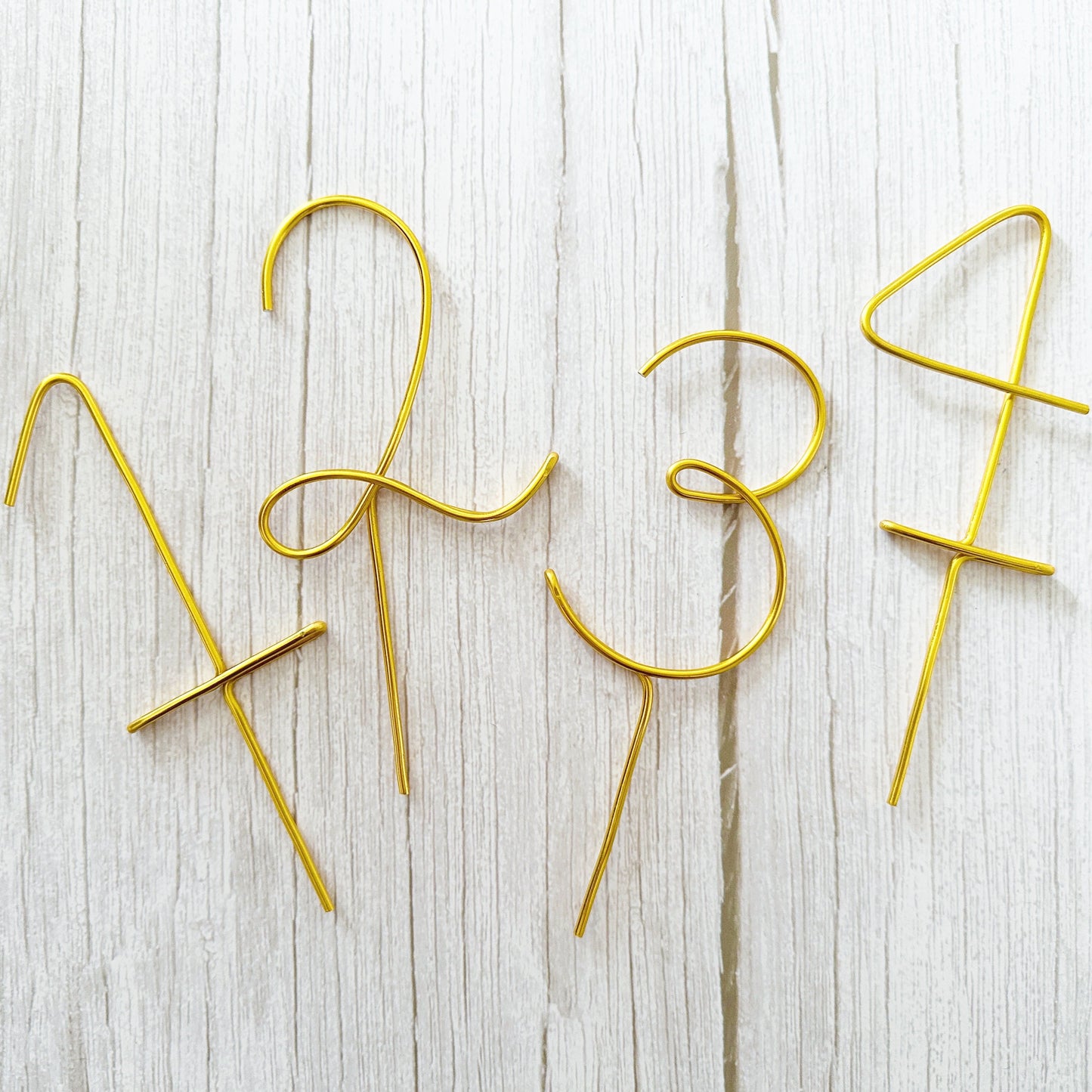 Gold cake toppers shaped like numbers 2, 3, and 4 on a light wooden surface.