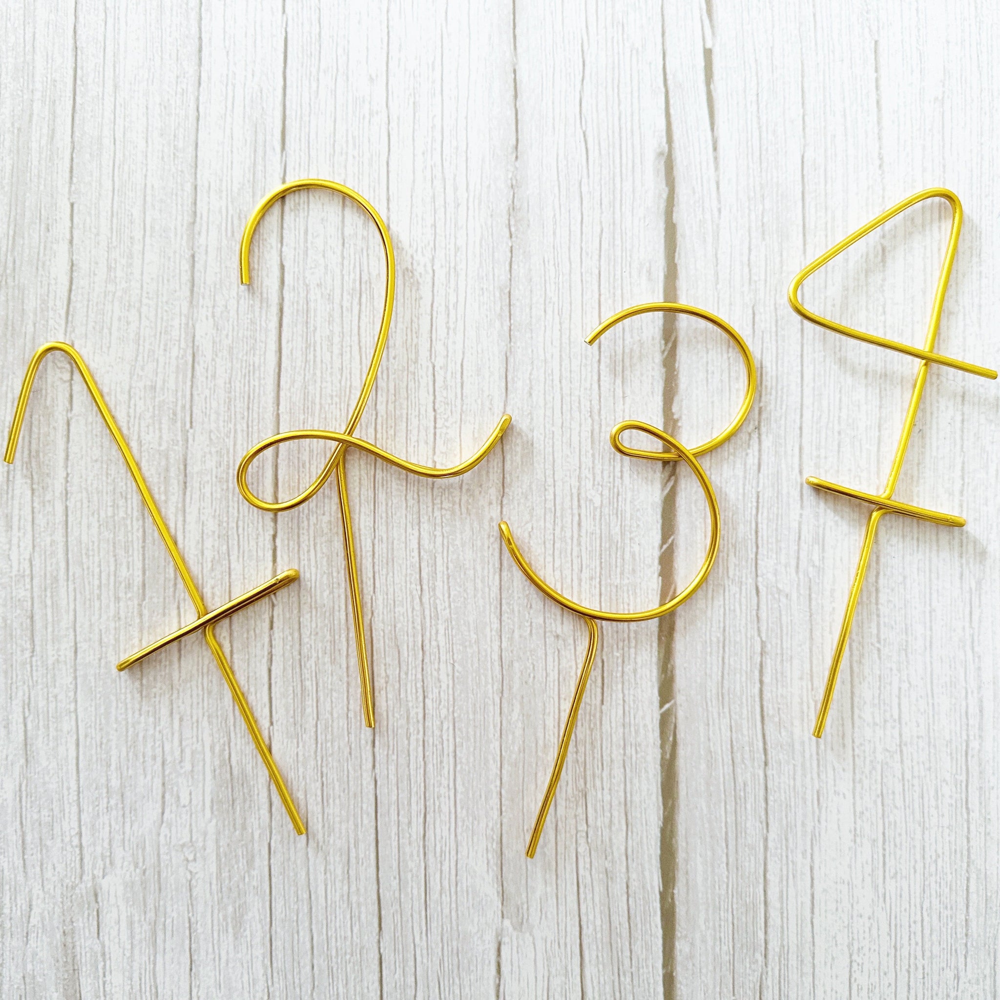 Gold cake toppers shaped like numbers 2, 3, and 4 on a light wooden surface.
